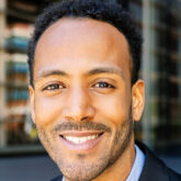Confident young latin american business man in suit smiling at camera sitting at staircase building entrance. Successful people